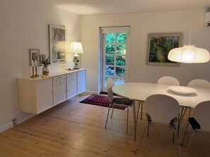 A dining area with a white table, chairs, a cabinet, and a door leading outside. - Idyllically situated wooden house by the forest (Viborg)