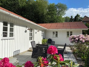 A white building with a red-tiled roof, outdoor seating area with wicker furniture, and flowering plants. - Idyllically situated wooden house by the forest (Viborg)