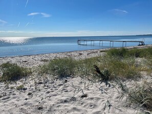 Une plage avec une jetée qui s’avance dans l’eau, des dunes de sable et une végétation clairsemée.