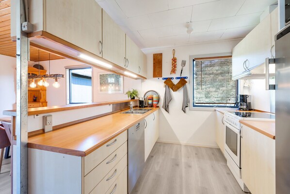 Une cuisine moderne avec des plans de travail en bois, des appareils en acier inoxydable et des luminaires suspendus.