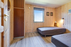 A room with wooden walls, a window, a bed, a wardrobe, and a bedside lamp.
