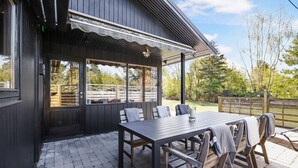 Une terrasse extérieure avec une table et des chaises en bois, un espace salon couvert et une vue sur le paysage environnant.