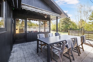 An outdoor patio with a wooden table and chairs, a covered seating area, and a view of the surrounding landscape.