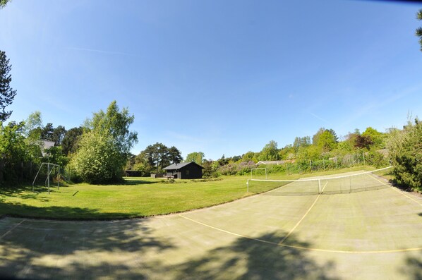 A tennis court with a net, surrounded by trees and a small building.