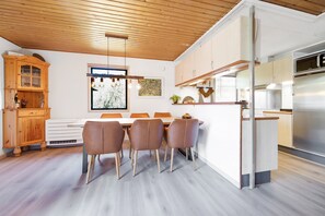 A modern kitchen with a dining area, wooden ceiling, and a large refrigerator.