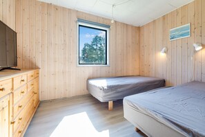 Ein Schlafzimmer mit Holzwänden, einem Fenster, einem Bett, einem Schminktisch und einem Fernseher.