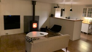 A modern living room with a fireplace, a flat-screen TV, a sofa, a dining table, and a kitchen area. - Quietly located holiday home close to the sea (Brenderup)