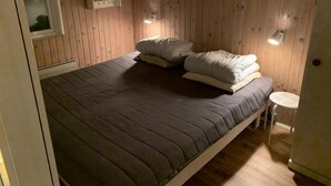 A single bed with a grey mattress and white pillows, a small bedside table, and a wall-mounted shelf. - Quietly located holiday home close to the sea (Brenderup)