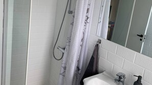 A bathroom with a shower, a sink, a mirror, and patterned tiles. - Quietly located holiday home close to the sea (Brenderup)