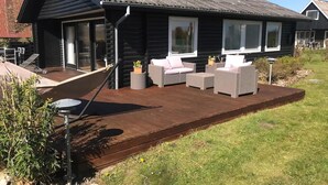 A log cabin with a deck, wicker furniture, and a garden. - Quietly located holiday home close to the sea (Brenderup)