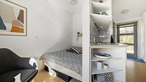 A compact room with a bed, a sofa, a built-in shelf with storage, and a window.