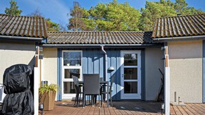 A house with a tiled roof, a covered patio with a table and chairs, and a covered grill.