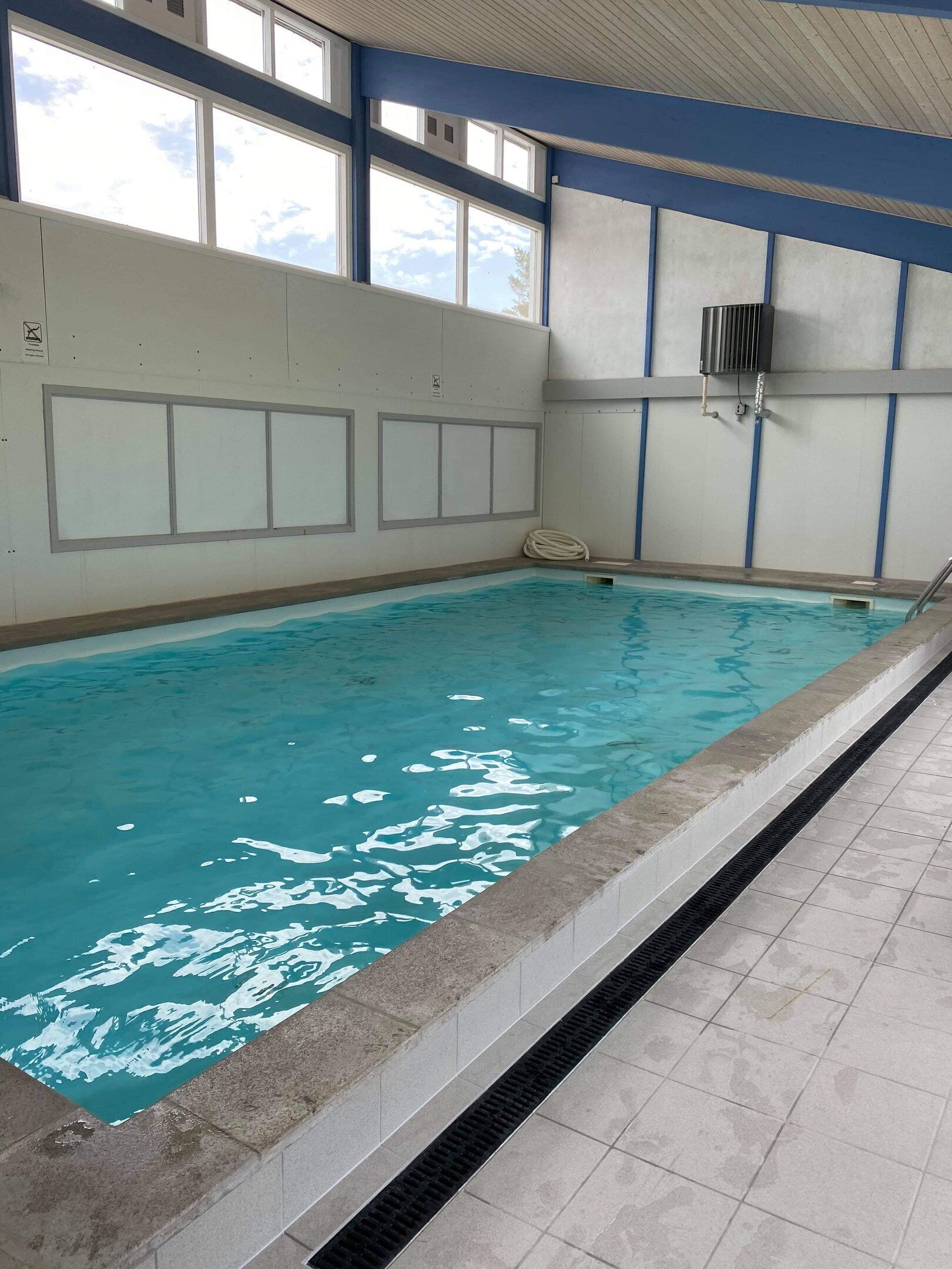 Une piscine intérieure à l’eau claire, dotée d’un sol carrelé et d’un mur vitré.