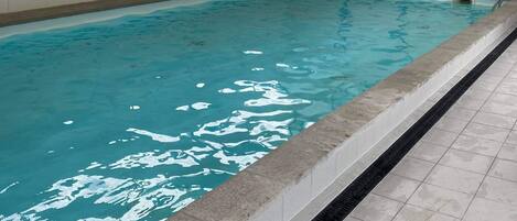 Une piscine intérieure à l’eau claire, dotée d’un sol carrelé et d’un mur vitré.