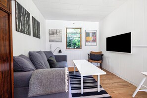 A modern living room with a grey sofa, a white table, a black and white striped rug, and a TV mounted on the wall. - Beautiful summer house near forest and beach (Højby)