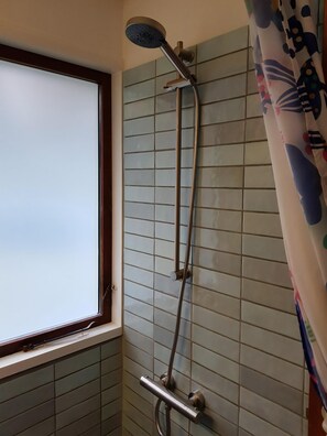 A shower with a handheld showerhead, a wall-mounted control panel, and a window with a view. - Beautiful summer house near forest and beach (Højby)
