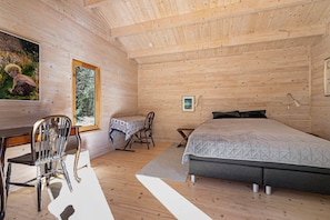 A wooden cabin interior with a bed, a desk, a chair, and a window.