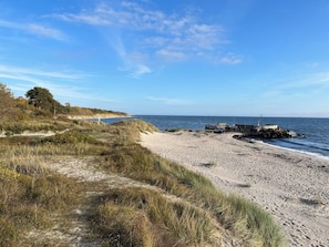 A beach with a sandy path, grassy dunes, and a rocky breakwater extending into the sea. - Architect-designed home on Bornholm (Aakirkeby)