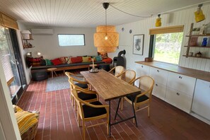 Un interior acogedor con una mesa de comedor de madera, sillas de mimbre, un banco y una lámpara de fibra trenzada grande.