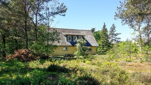 Una casa amb teulada inclinada, envoltada de vegetació abundant i arbres.