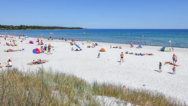 Platja amb tendes de campanya, persones prenent el sol i embarcacions a l'aigua.