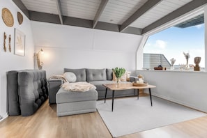 En moderne stue med en grå sofa, et træbord og et stort vindue.
