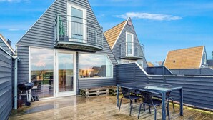 A residential deck with a table and chairs, a barbecue grill, and a sliding glass door leading to an interior space. - Family holiday with sea view in Gedser Feriepark (Gedser)