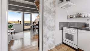 A modern kitchen with a large window, a dining area with a view, and a built-in oven. - Family holiday with sea view in Gedser Feriepark (Gedser)