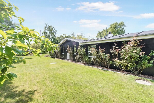 A residential property with a well-maintained lawn, a wooden fence, and a house with a dark exterior.