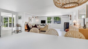A spacious living area with a white dining table, comfortable seating, a television, and a large window offering a view of greenery. - Unique holiday home in quiet surroundings (Storvorde)