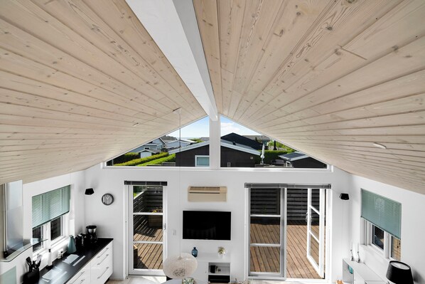 A modern kitchen with a large window, a flat-screen TV, and a wooden ceiling.