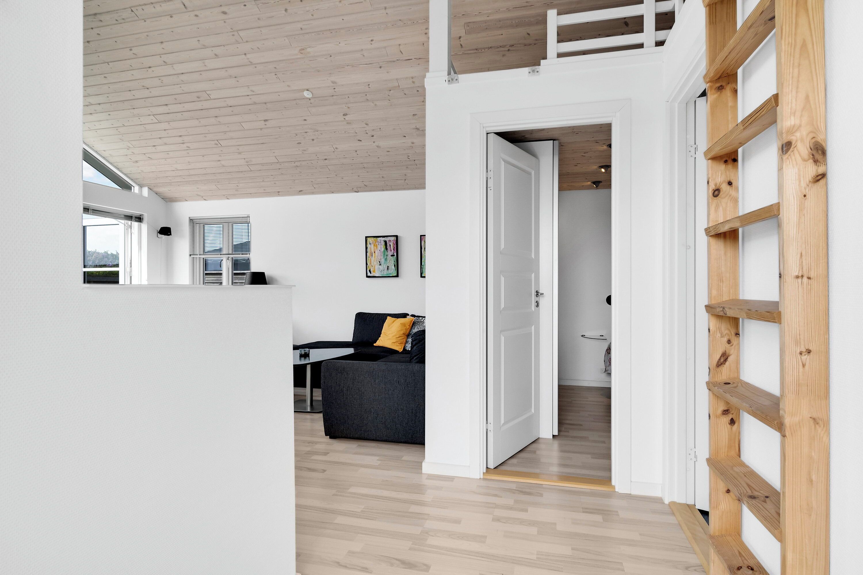 A modern interior with a wooden ceiling, a grey sofa with a yellow pillow, and a white door leading to another room.