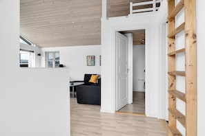 A modern interior with a wooden ceiling, a grey sofa with a yellow pillow, and a white door leading to another room.