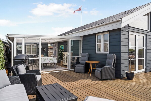 A covered patio with outdoor furniture, a grill, and a flag.