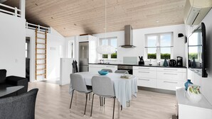 Et moderne køkken med hvide skabe, et rustfrit stål emfang og et spiseområde med et bord og stole.