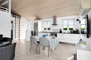 A modern kitchen with white cabinets, a stainless steel range hood, and a dining area with a table and chairs.