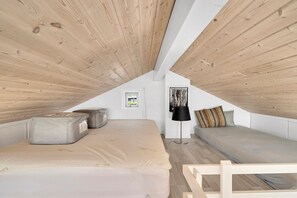 Un dormitorio tipo loft con techo inclinado, cama, sofá, lámpara y ventana.