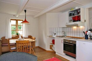 Uma cozinha compacta com área de refeições, móveis de madeira, luminária pendente vermelha e forno embutido.