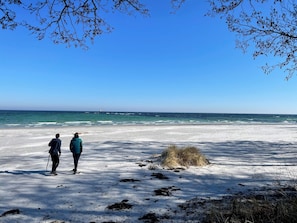 Uma praia com duas pessoas em pé, céu claro e o oceano ao fundo.