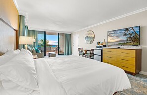 Une chambre d’hôtel avec un grand lit, un bureau avec une chaise, une télévision et une vue sur l’océan.
