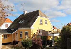 A yellow house with a steep roof, a small porch, and a staircase leading to the entrance.