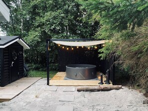 A hot tub under a wooden pergola with string lights, surrounded by a garden and a wooden deck. - Authentic holiday home close to the beach (Væggerløse)