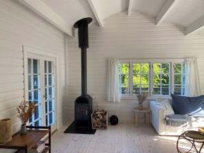 Una habitación con estufa de leña, un sofá blanco, una mesita y una ventana con cortinas.
