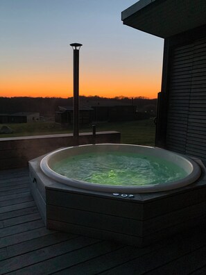 Et spabad på en træterrasse med solnedgang i baggrunden.