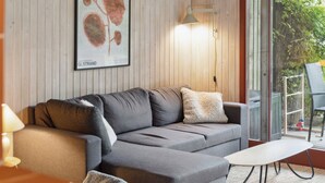 Ett modernt vardagsrum med en grå soffa, ett litet vitt bord och en inramad botanisk tavla på väggen.