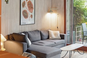 Ett modernt vardagsrum med en grå soffa, ett litet vitt bord och en inramad botanisk tavla på väggen.