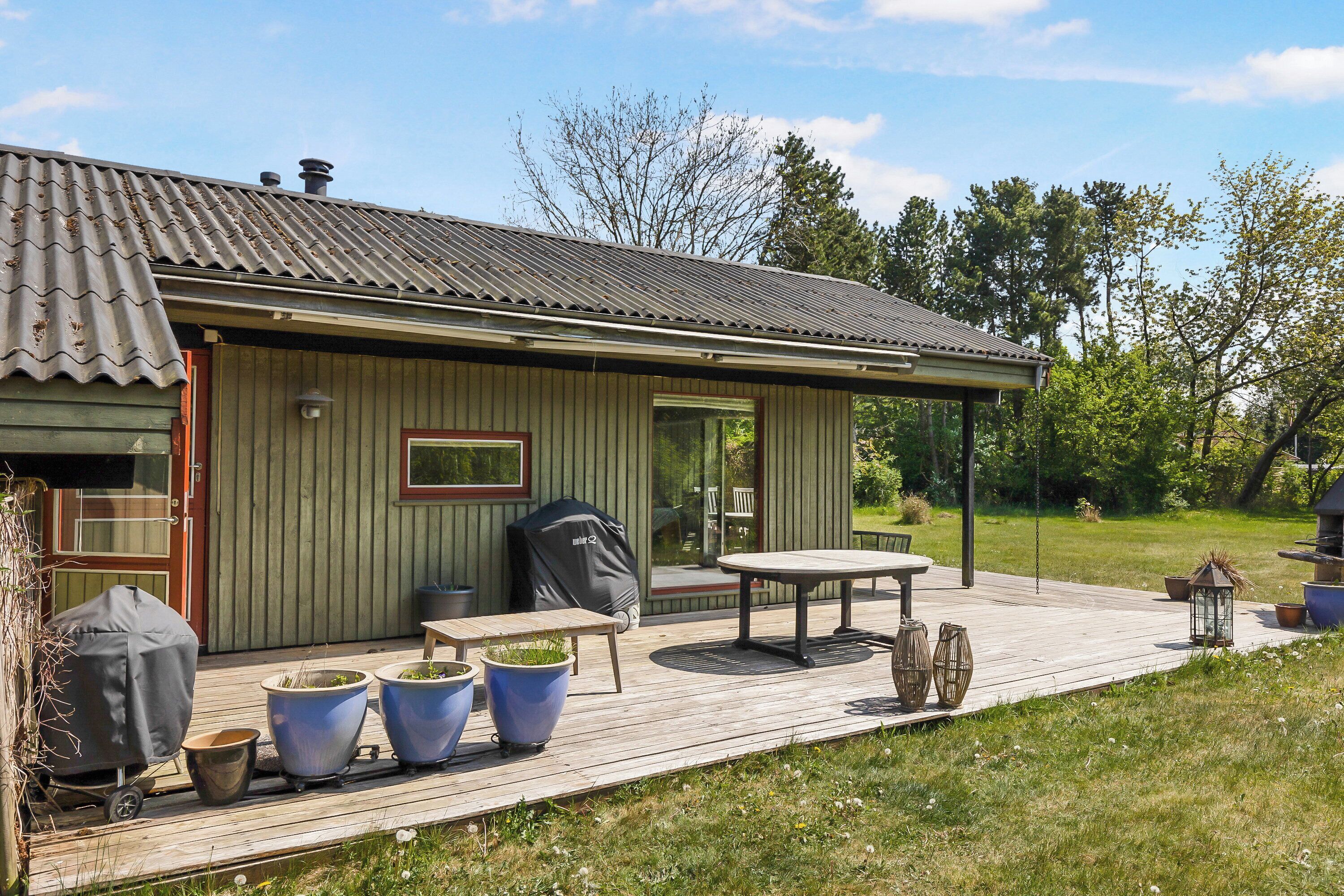 Eine Holzterrasse mit Tisch und Stühlen, einem Grill und Blumentöpfen.