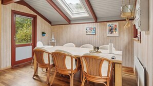 En matplats med ett träbord, flätade stolar, ett takfönster och utsikt över grönskan utanför.