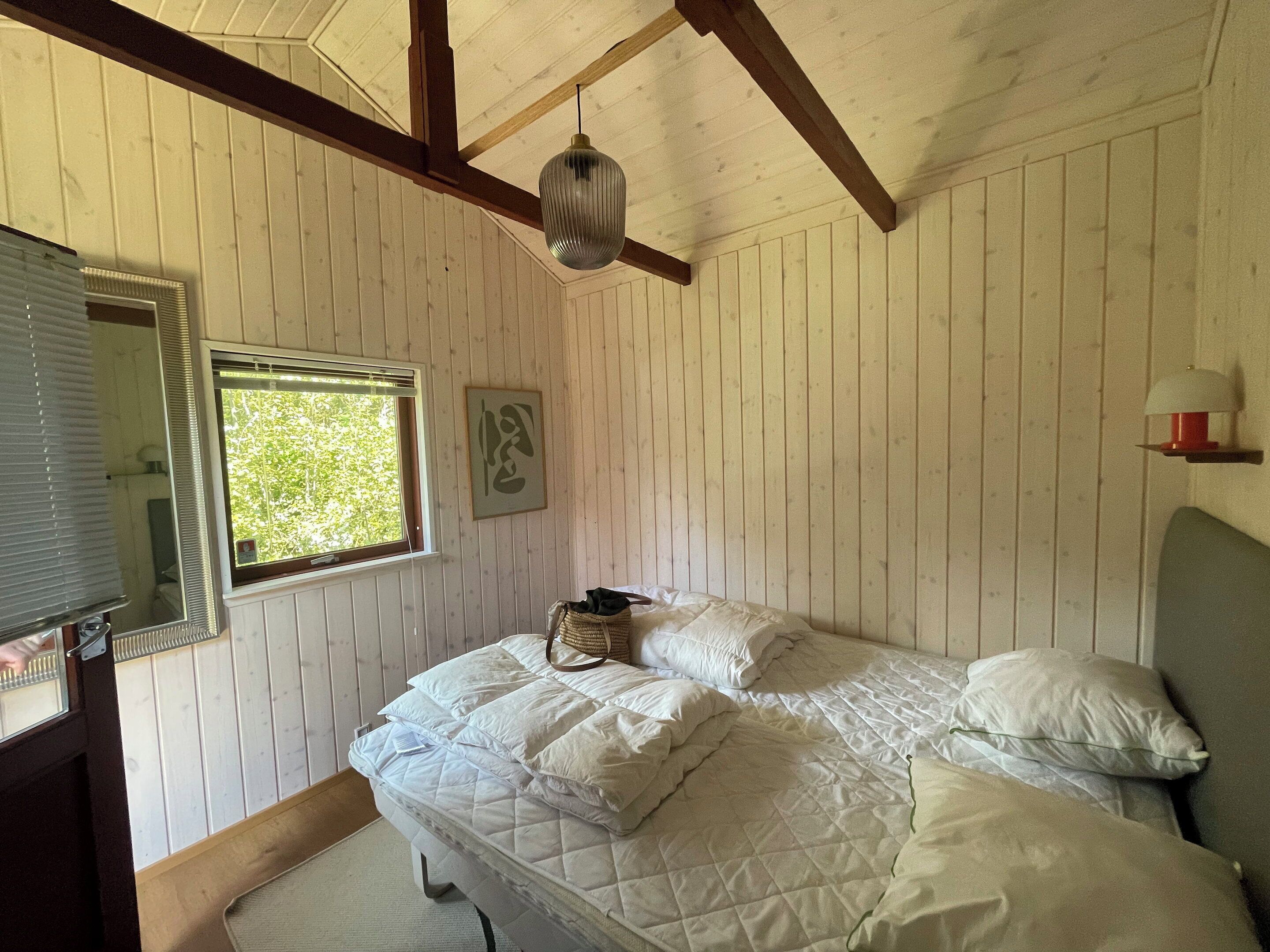 A bedroom with a bed, a window, a mirror, and a wall-mounted lamp.