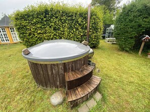 Ein Whirlpool mit Holzverkleidung und einem Metalldeckel, umgeben von Gras und einer Hecke.